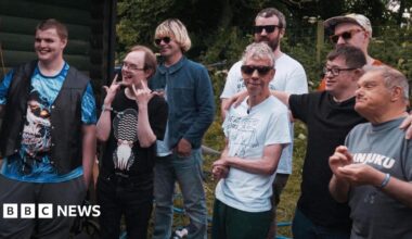 A mixed age group of men, some with disabilities, stand alongside each other smiling.