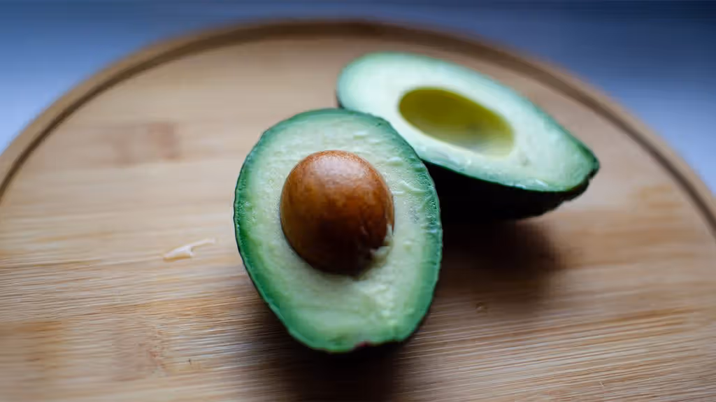 two avocado halves on a wooden chopping board