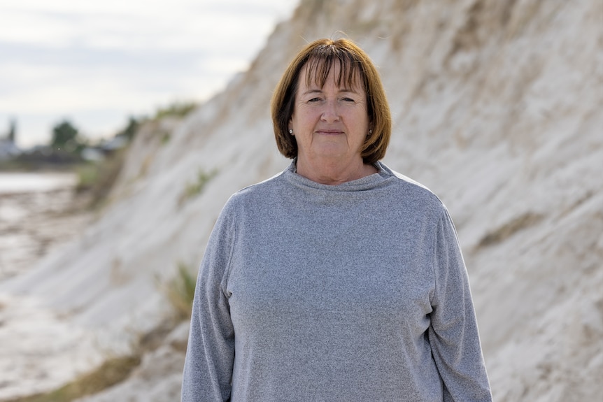 Linda Balcombe standing in front of an eroded sand dune, frowning 