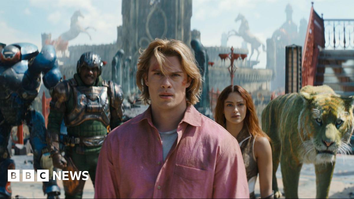 Masters of the Universe still. A group of superhero characters and a CGI lion are stood in a line in front of a tall building.