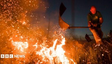 Firefighters tackle a wild fire on Winter Hill near Bolton in 2018. It is dark and the fire is a white hot blaze being batted by a fireman sending sparks into the sky