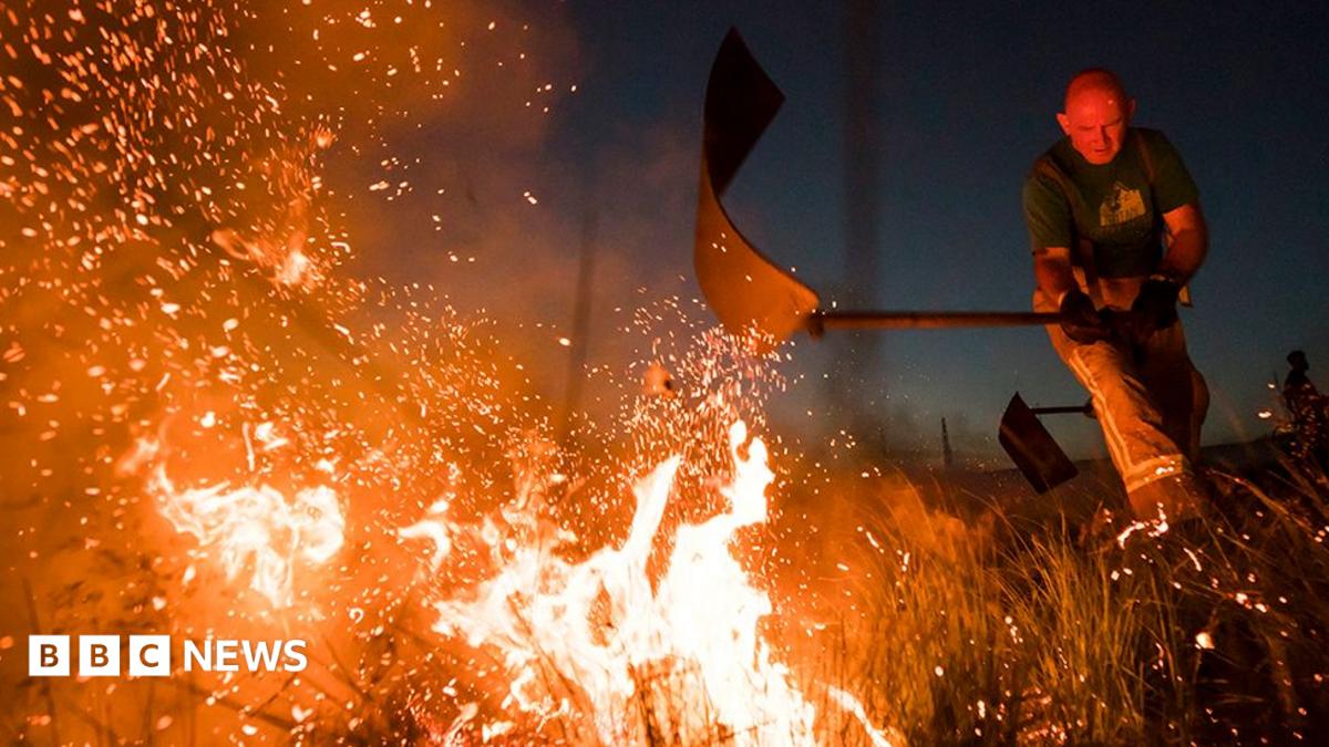 Firefighters tackle a wild fire on Winter Hill near Bolton in 2018. It is dark and the fire is a white hot blaze being batted by a fireman sending sparks into the sky