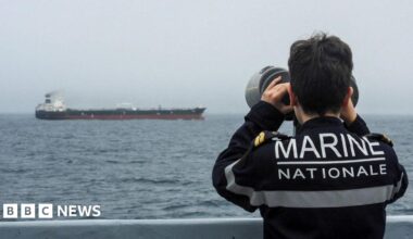 A French Navy officer wearing a black uniform labelled Marine Nationale observes an alleged Russian oil tanker sailing in the Atlantic ocean.