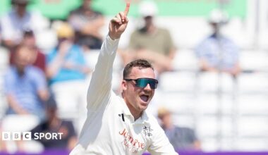 Liam Patterson-White celebrates taking a wicket by raising his right hand with his index finger pointing towards the sky.