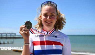 Zoe Backstedt in a British champion's jersey holds her gold medal on the sea-front at Aberystwyth