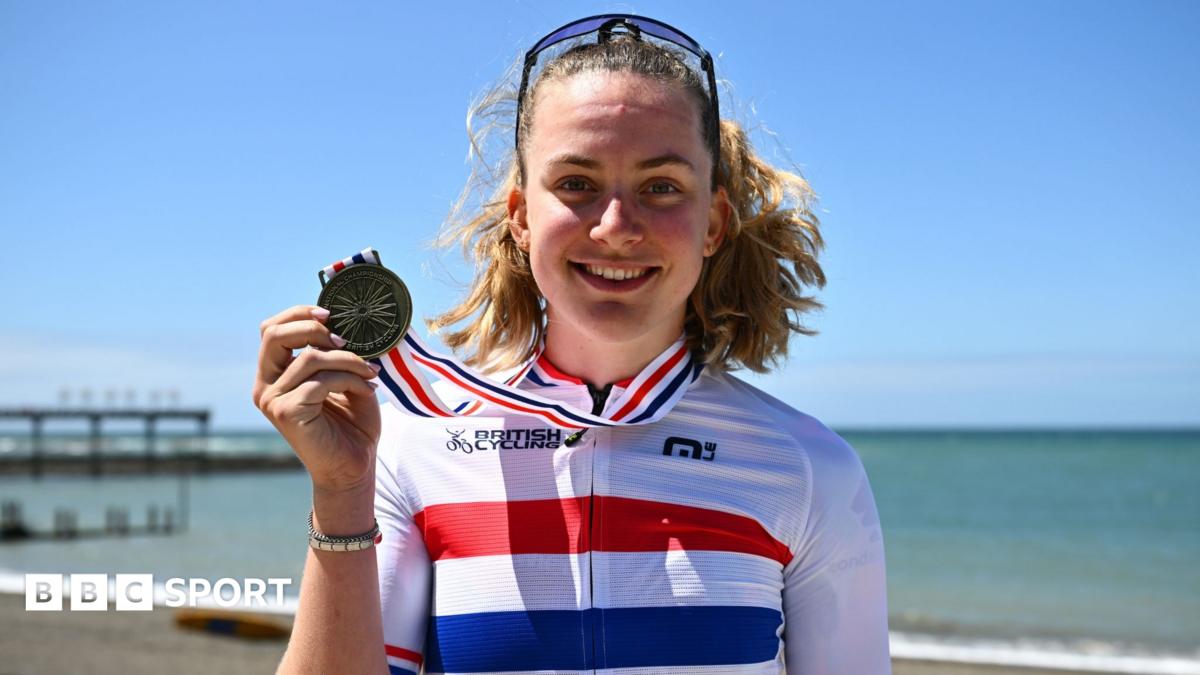 Zoe Backstedt in a British champion's jersey holds her gold medal on the sea-front at Aberystwyth