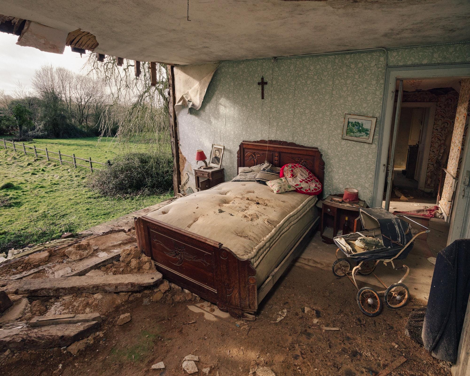 a photograph by Brendon Burton of a bedroom, the wall ripped open to the outside