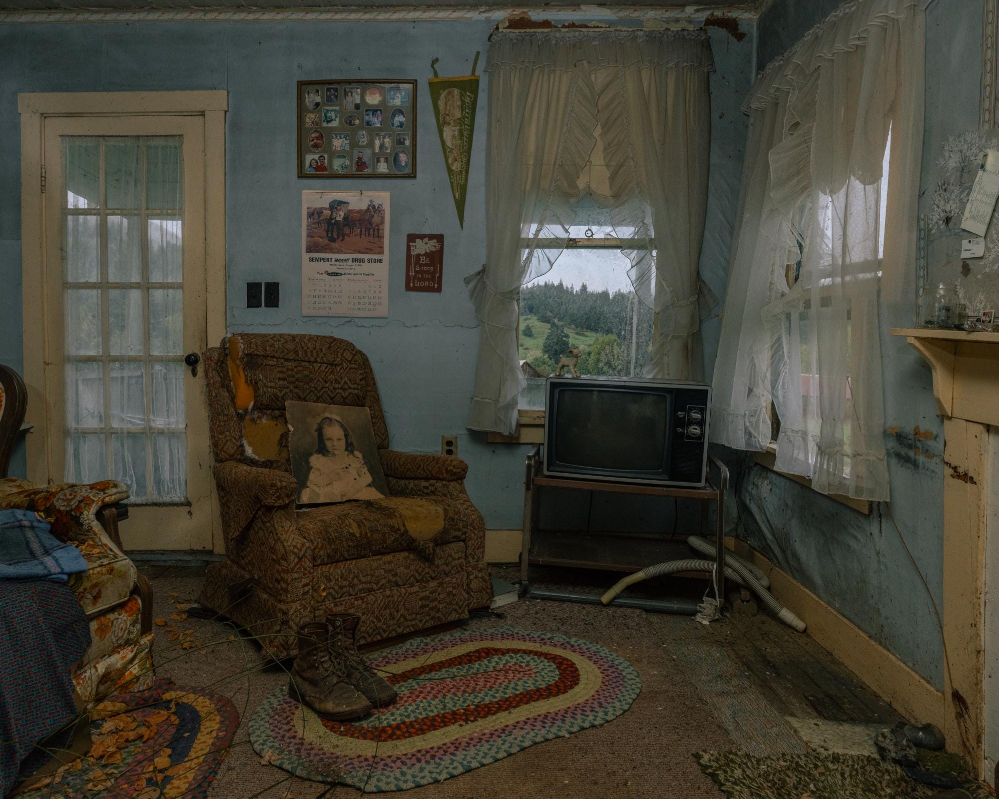 a photograph by Brendon Burton of the inside of an old living room with a reclines, blue wallpaper, and an old TV, V.