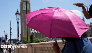 A person shielding from the Sun under an umbrella with the Houses of Parliament in the background