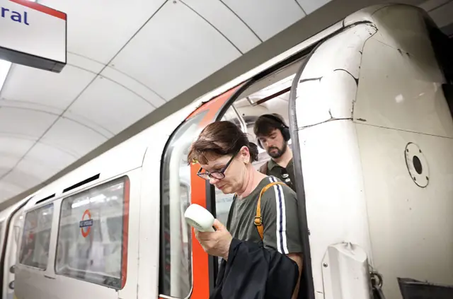 A woman holds a fan to her face as she gets off the tube