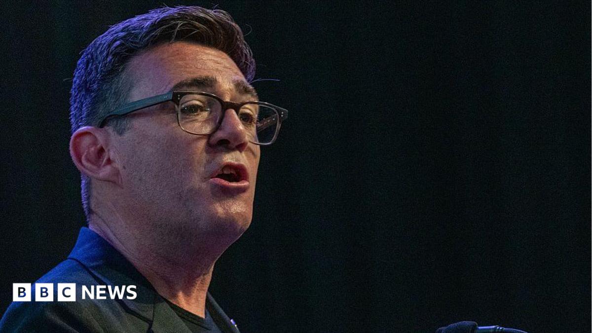 Andy Burnham wearing a black jacket with a black t-shirt talking to an audience with a black background behind him