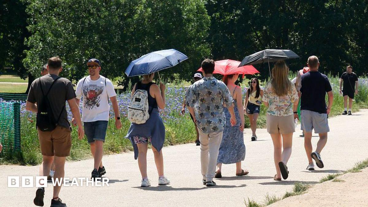 people walking on a pathway through a park.  Some are holding umbrellas to shade them from the hot weather