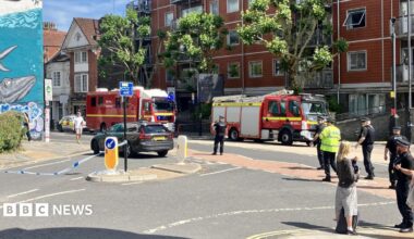 Two fire engines parked inside a cordon, with blue and white police tape securing a large section of the main road.