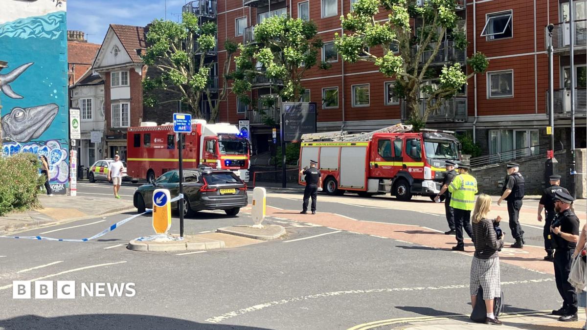 Two fire engines parked inside a cordon, with blue and white police tape securing a large section of the main road.