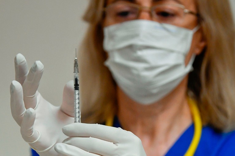 A masked medical professional prepares a syringe containing a dose of BCG vaccine.