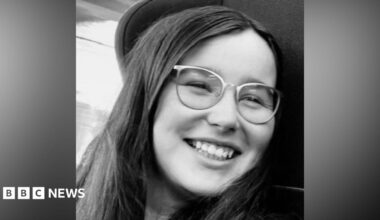 Close-up black-and-white photograph of Jess Turnbull. She is smiling as she looks to her left. She has long dark hair and is wearing glasses.
