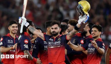 Virat Kohli holds his bat and helmet aloft as his RCB team-mates celebrate winning the IPL
