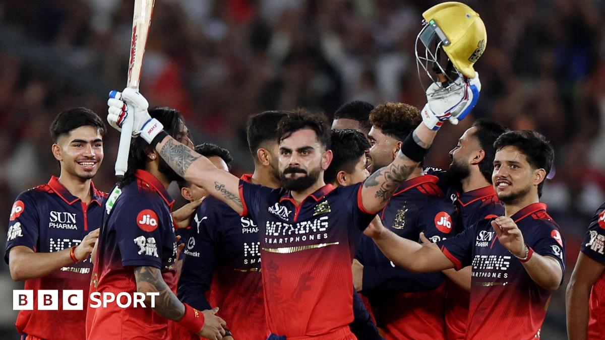 Virat Kohli holds his bat and helmet aloft as his RCB team-mates celebrate winning the IPL