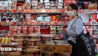 A customer walking past a row of shelves filled to the brim with instant noodles at a supermarket in Japan.