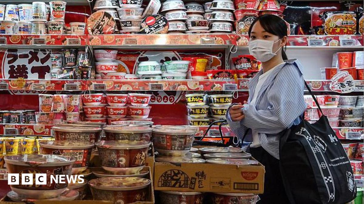 A customer walking past a row of shelves filled to the brim with instant noodles at a supermarket in Japan.