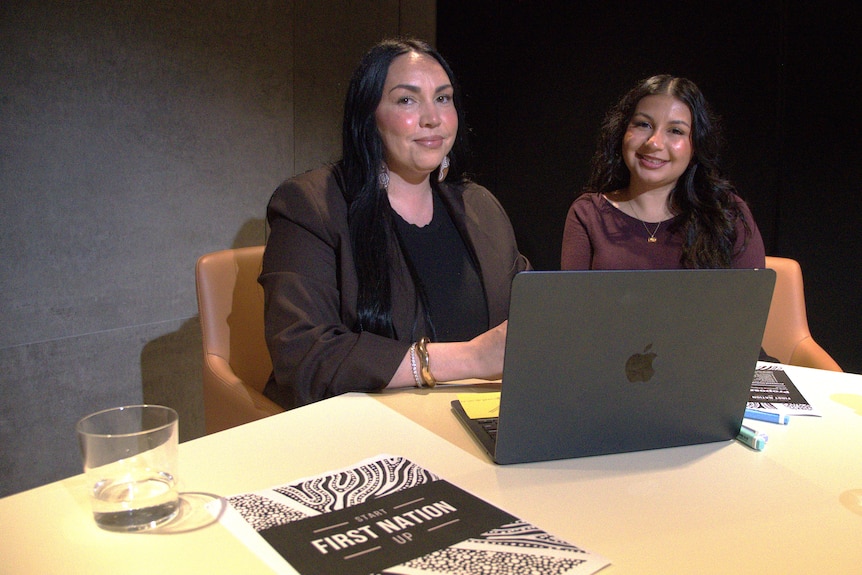 Sinead is sitting next to another woman at a desk with a laptop and paperwork in front of them