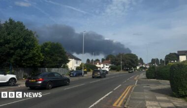 A large plume of smoke can be seen from a pavement at the side of a road in Liverpool.