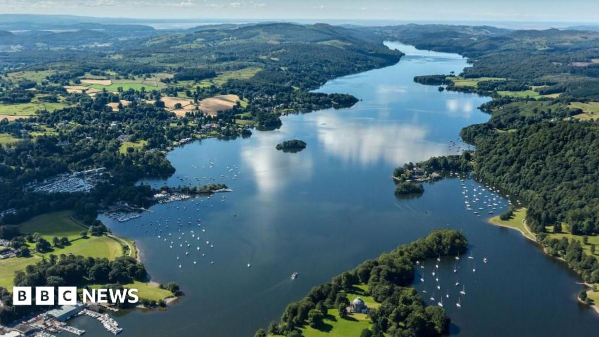 An aerial view of Windermere, England's largest lake which stretches into the distance narrowing as it goes. Boats can be seen dotted along its foreshore