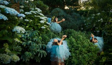 a photograph by Tamara Dean of three individuals sitting in a dense brush, wearing blue tutus around their bodies, only their arms sticking out