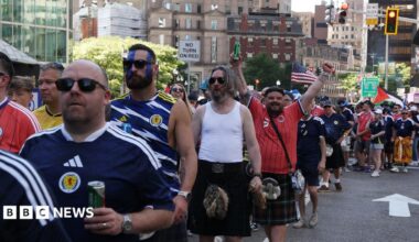Men in blue or red Scotland strip, many in kilts, queue on an American street