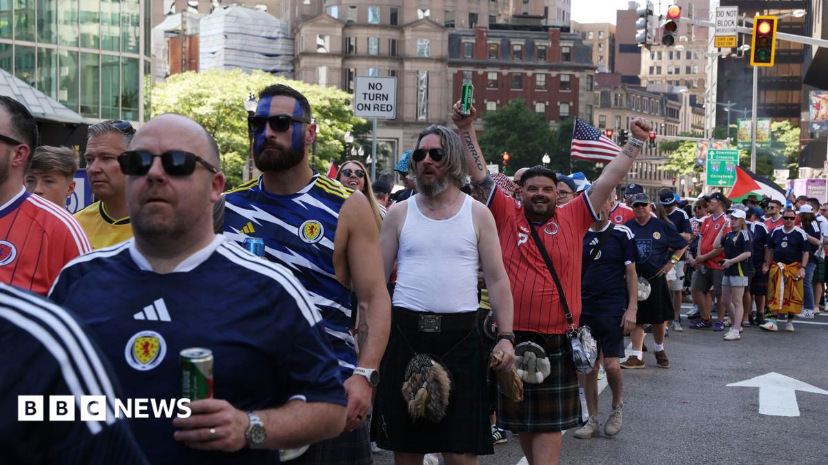 Men in blue or red Scotland strip, many in kilts, queue on an American street
