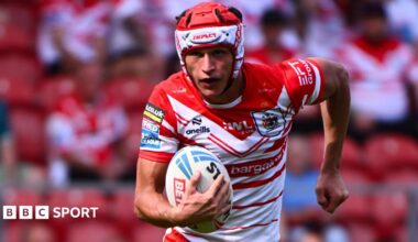 Harry Robertson, wearing St Helens' red and white jersey, runs with a rugby league ball in his right hand