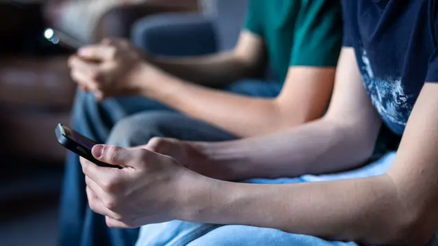 Two teenage boys look at their smartphone screens.