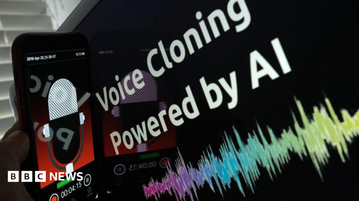 This picture is has a touchscreen mobile phone being held next to a screen which reads "voice cloning powered by AI".  The mobile phone screen display has a animated radio microphone with a red background. The lower third of the mobile phone screen has a record button and a timing display.
