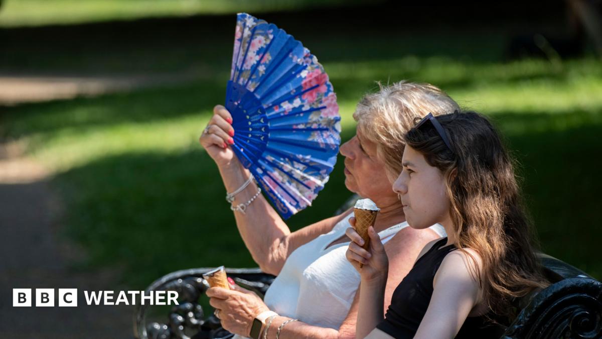 two women sitting on a park bench.  One eating an ice cream, the other fanning herself in the hot weather