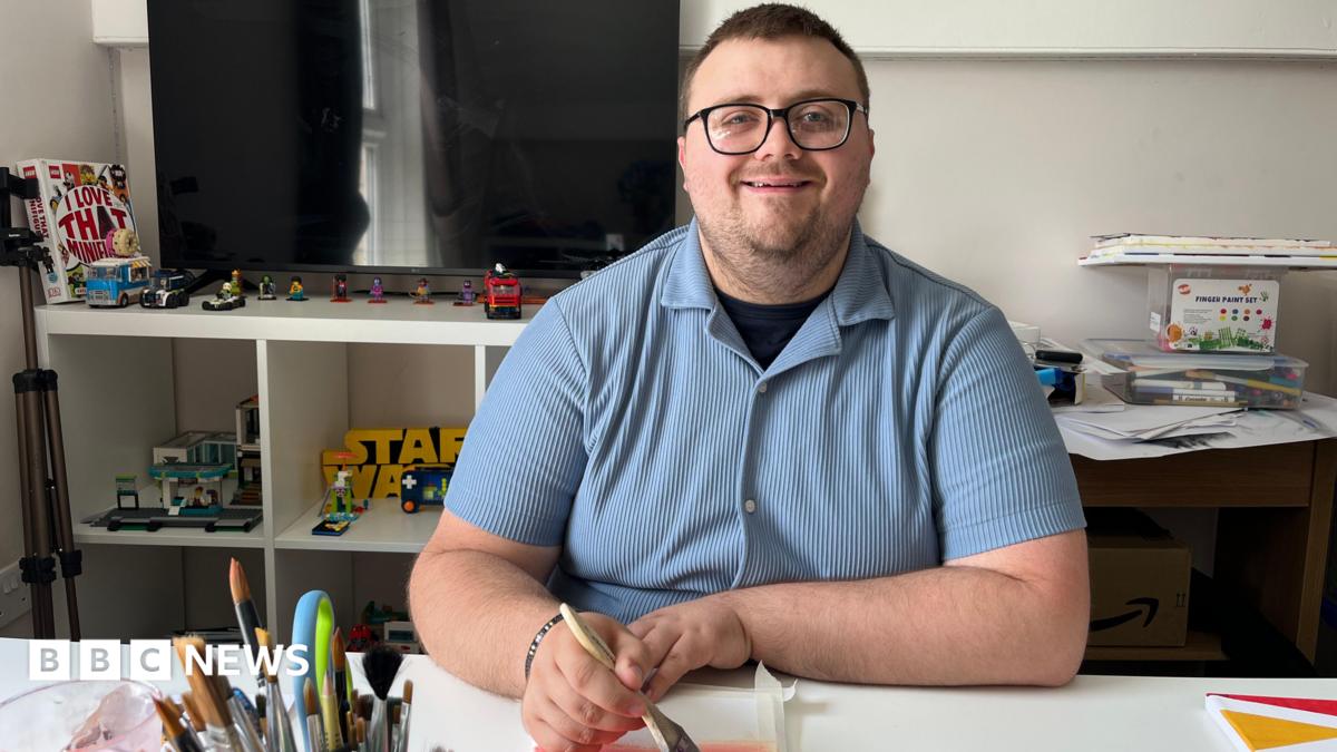 A man in a blue striped shirt sat painting at a table