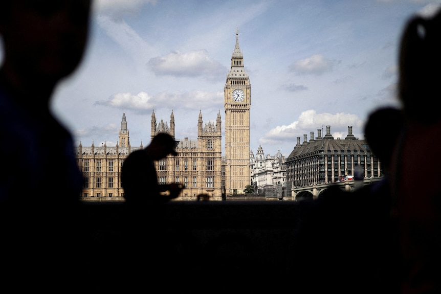 The UK Houses of Parliament and Big Ben as seen from across the River Thames, with a man's silhouette in the foreground.