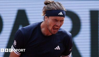 Alexander Zverev, wearing a black Adidas t-shirt and headband with his hair tied back, roars with his mouth open