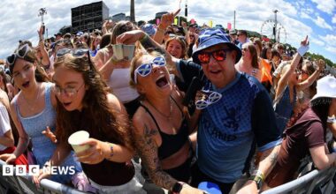 Fans screaming and singing on a sunny day. One of the fans is wearing sunglasses with a saltire design.