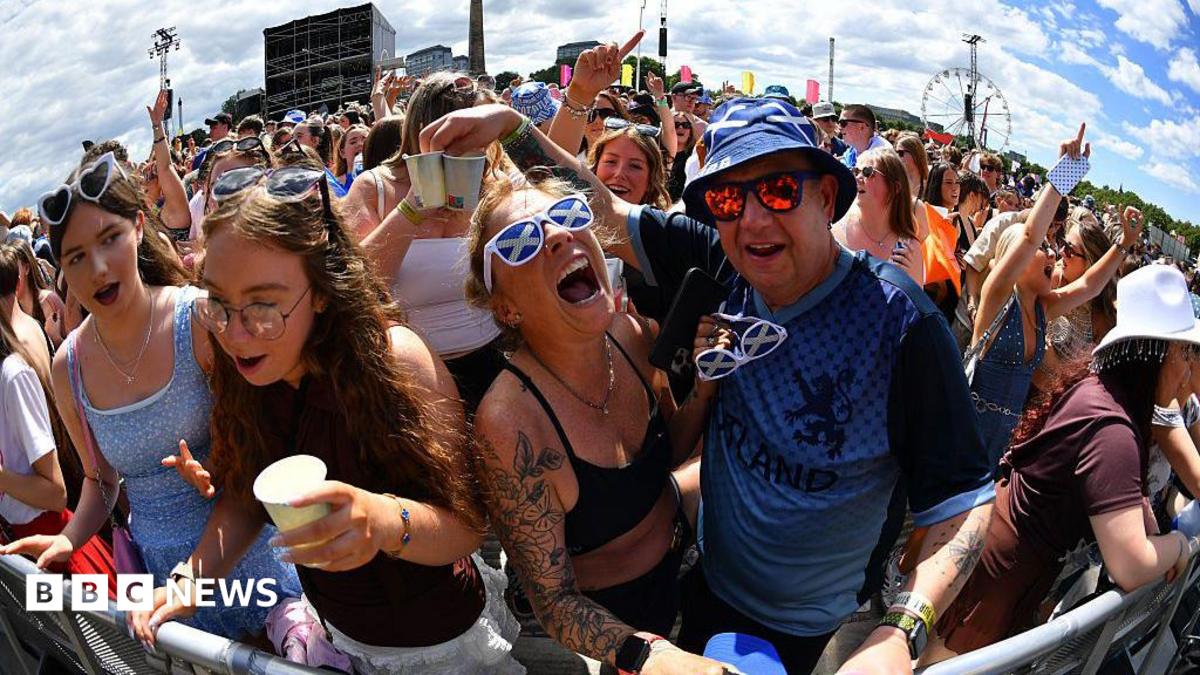 Fans screaming and singing on a sunny day. One of the fans is wearing sunglasses with a saltire design.