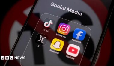 TikTok, Instagram, Facebook, X, Snapchat and YouTube apps displayed on an iPhone screen under a "social media" tab, with an icon used to show under-16s banned reflected across it.