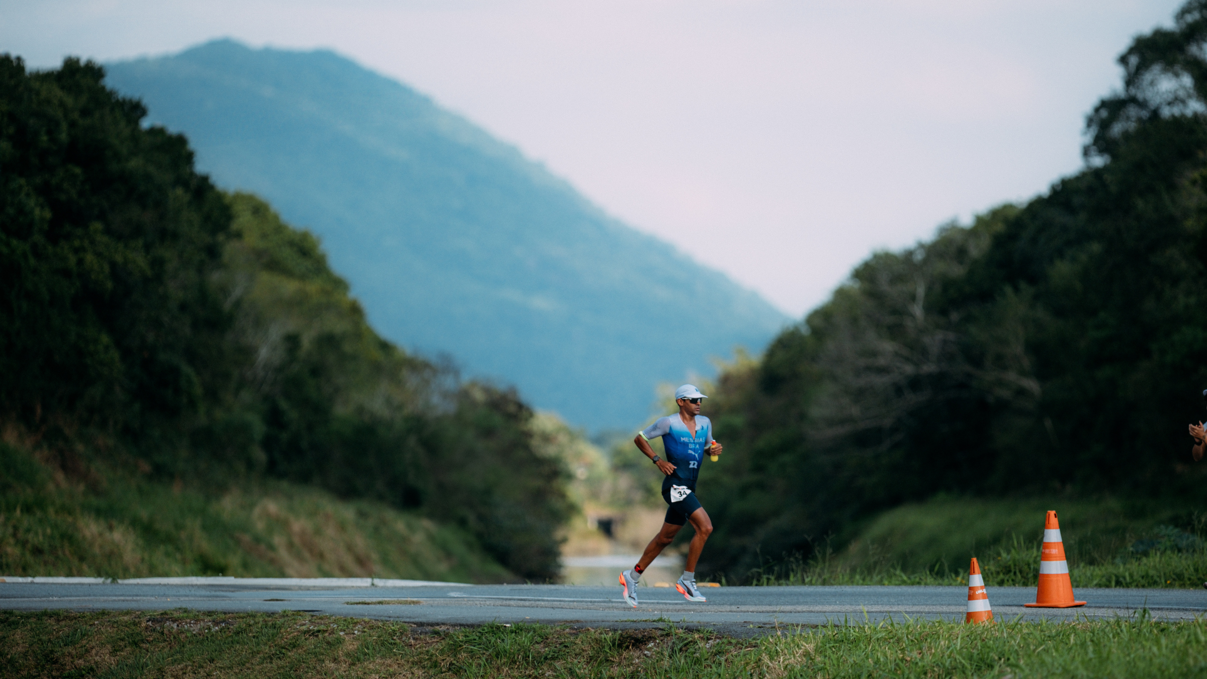 man running on road outside in between hills and trees at Ironman 70.3 Florianopolis