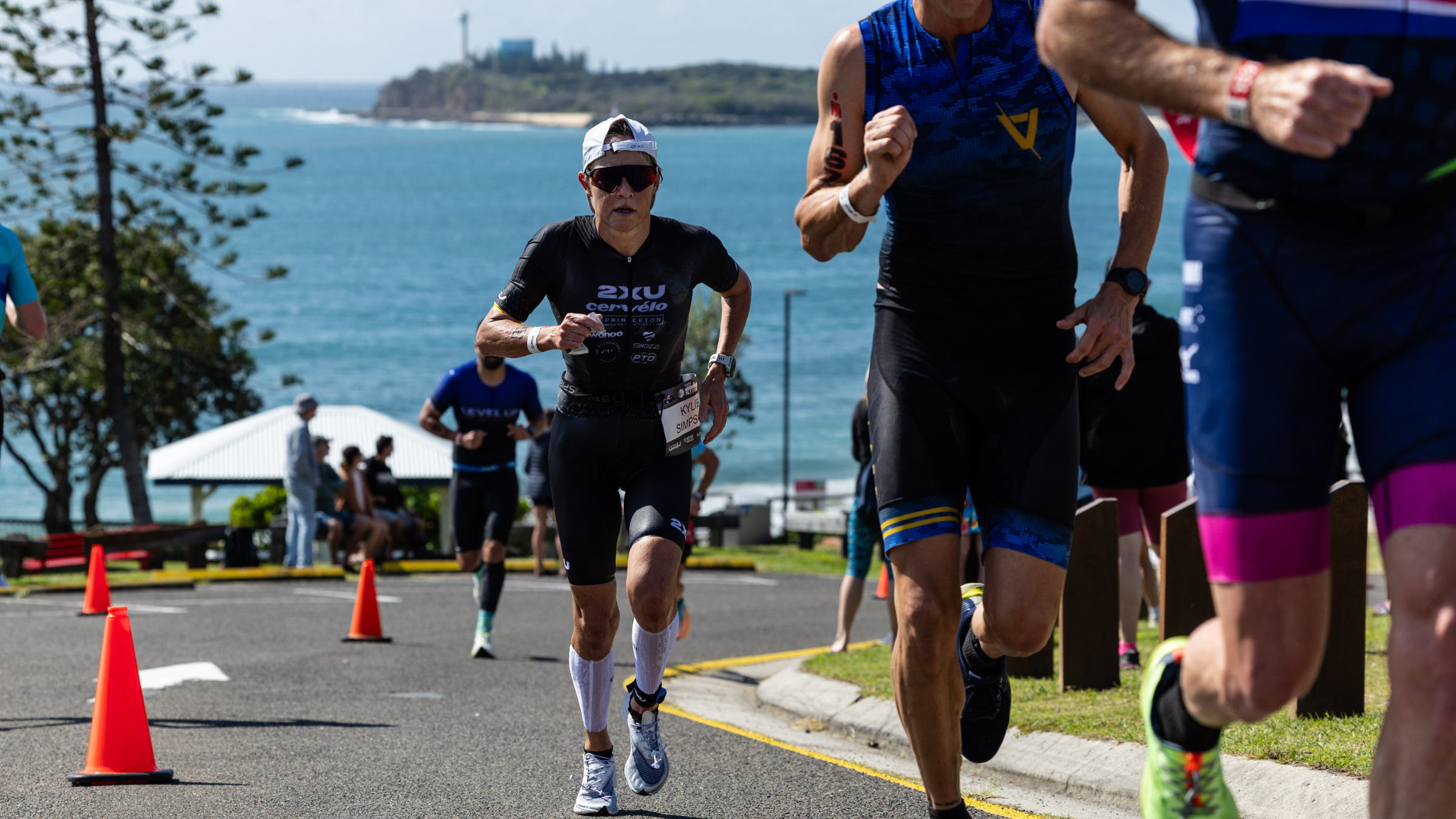 athletes run uphill toward camera on a road with island and water in the background at Ironman 70.3 Sunshine Coast