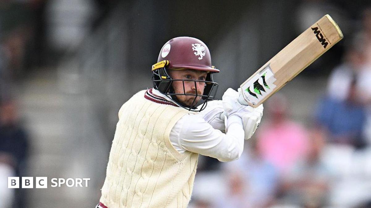 Lewis Goldsworthy in white cable jumper and maroon batting helmet holds his bat up to his right as he plays a shot
