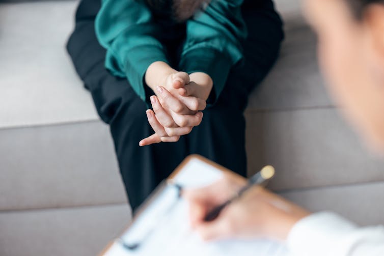 A woman clasping her hands in a therapy session