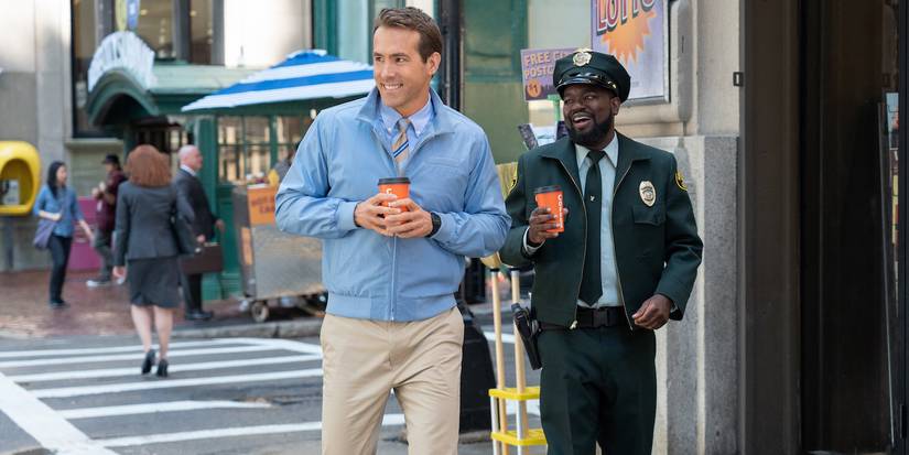 Ryan Reynolds and Lil Rel Howery walking on a city street and smiling at someone off to the side in Free Guy.