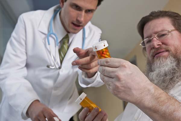 A man holds a bottle of prescription medication capsules as a doctor points to the bottle, explaining dosage.