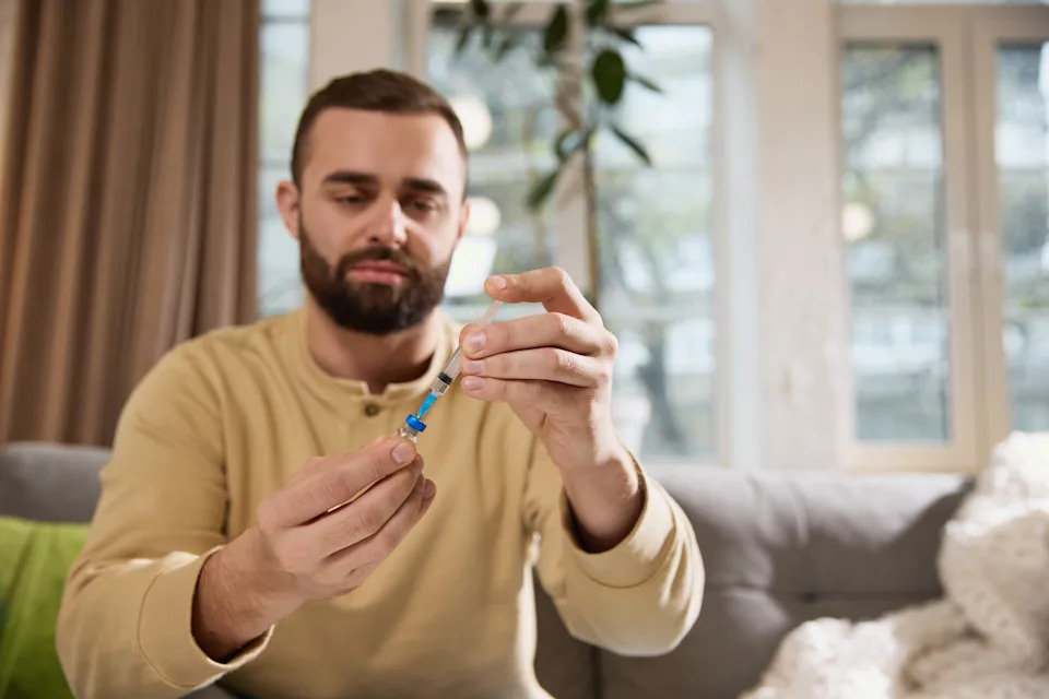 Person drawing medication from a vial into a syringe at a kitchen table