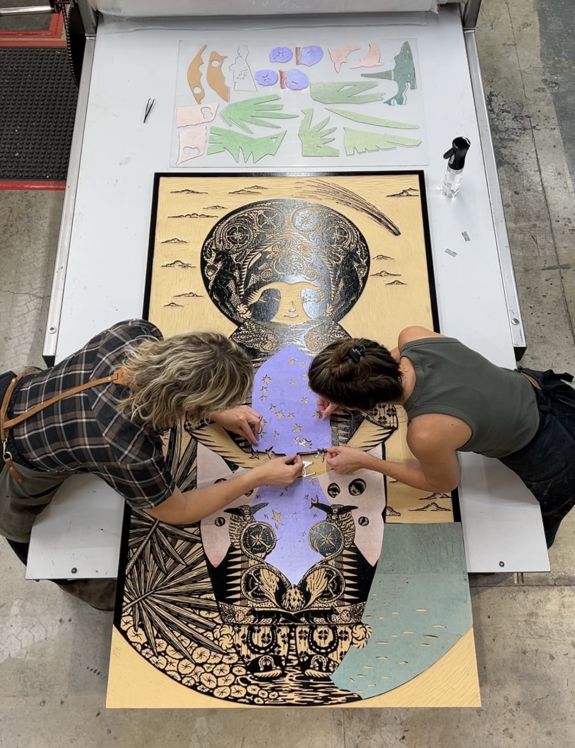 two artists collaging paper onto a large carved woodblock