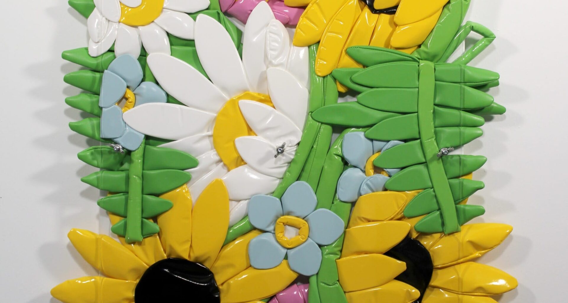 an artwork of cartoonish sculptural flowers made of poylurethane that are squished between two panels of Plexiglas