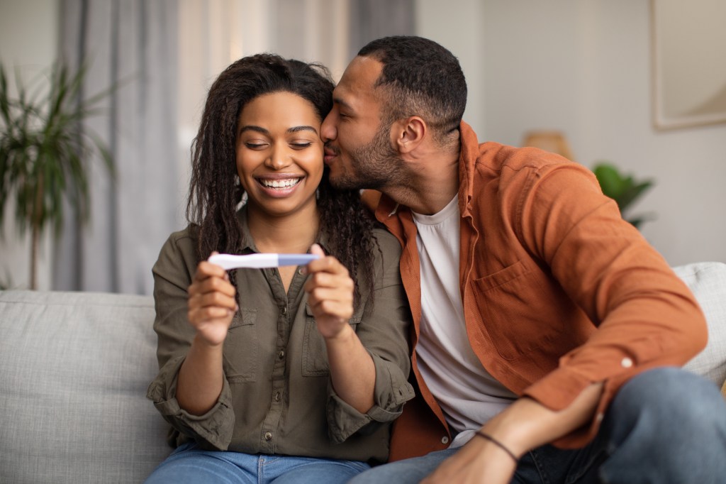 Happy African American couple holding a positive pregnancy test at home.